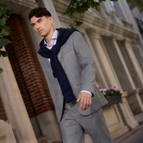 Un homme portant un veston sport gris, une chemise grise et une écharpe noire.