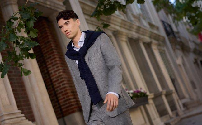 A man wearing a grey sport jacket with grey shirt and black scarf