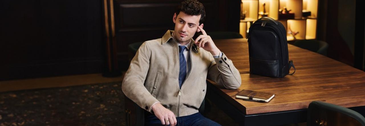 A man wearing a light brown Suede jacket, blue tie and jeans