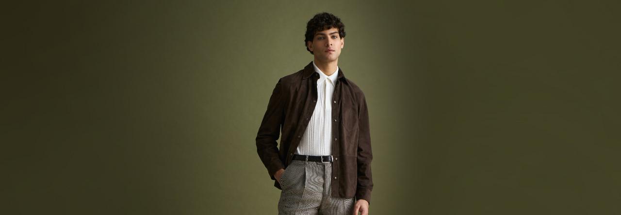 A man wearing a dark brown Suede overshirt with white polo t-shirt and grey pants