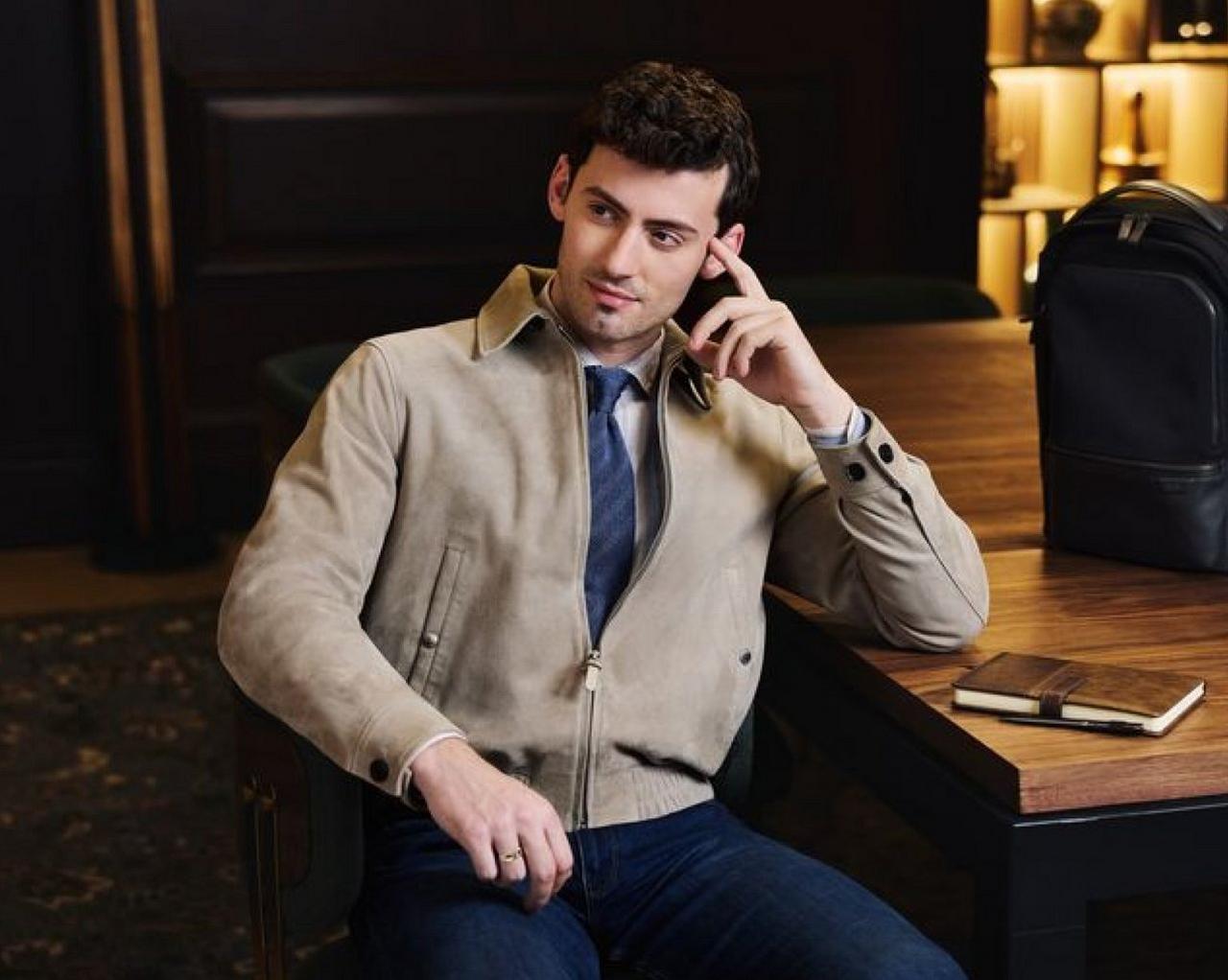 A man wearing a light brown Suede jacket, blue tie and jeans