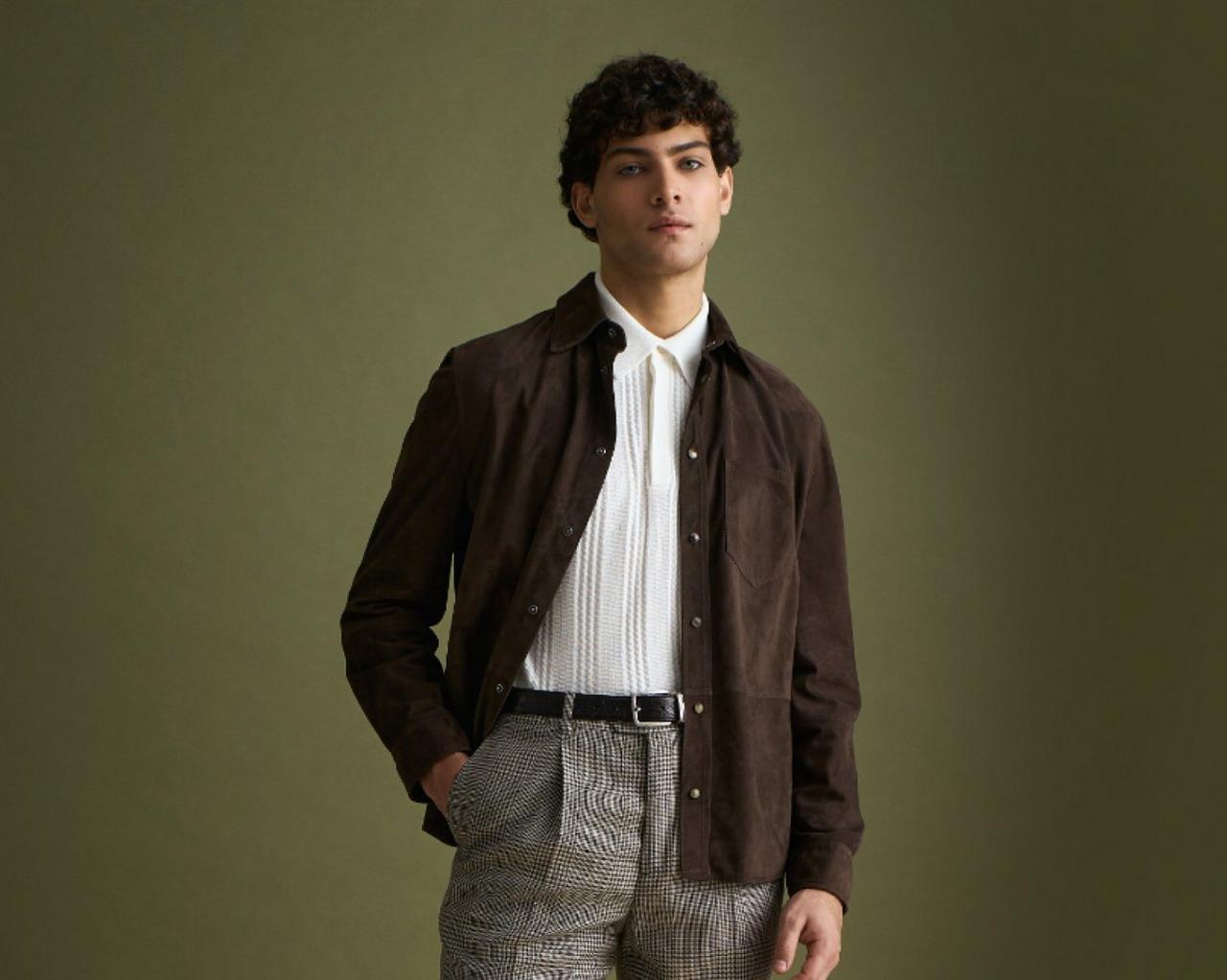A man wearing a dark brown Suede overshirt with white polo t-shirt and grey pants