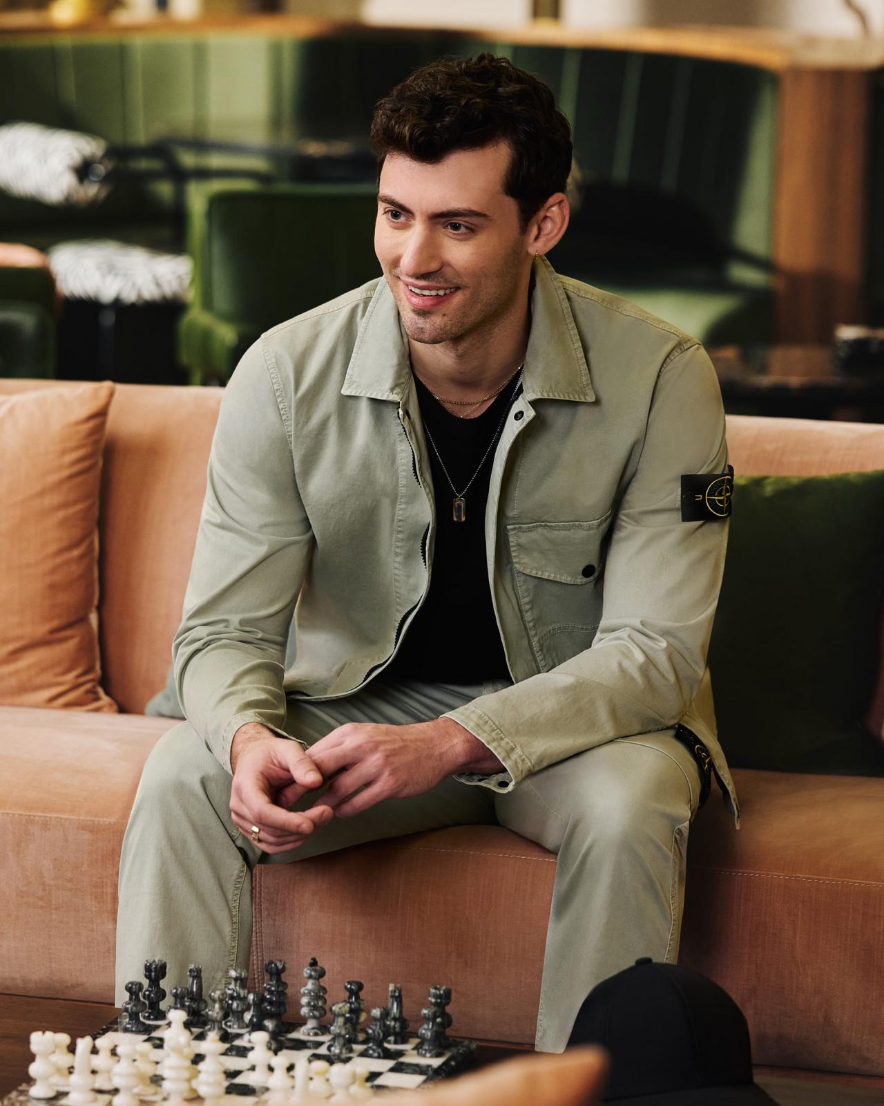 A man wearing a sage green Stone Island overshirt styled with a black shirt and coordinated pants