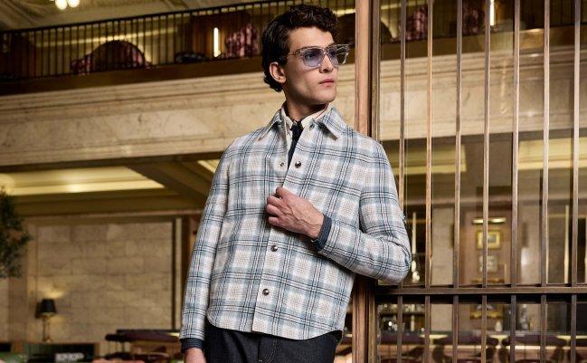 A model wearing a plaid light blue and off-white Thom Browne overcoat styled with dark denim