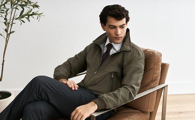 Male model lounging in a forest green Tom Ford jacket, styled with a white dress shirt, and patterned tie