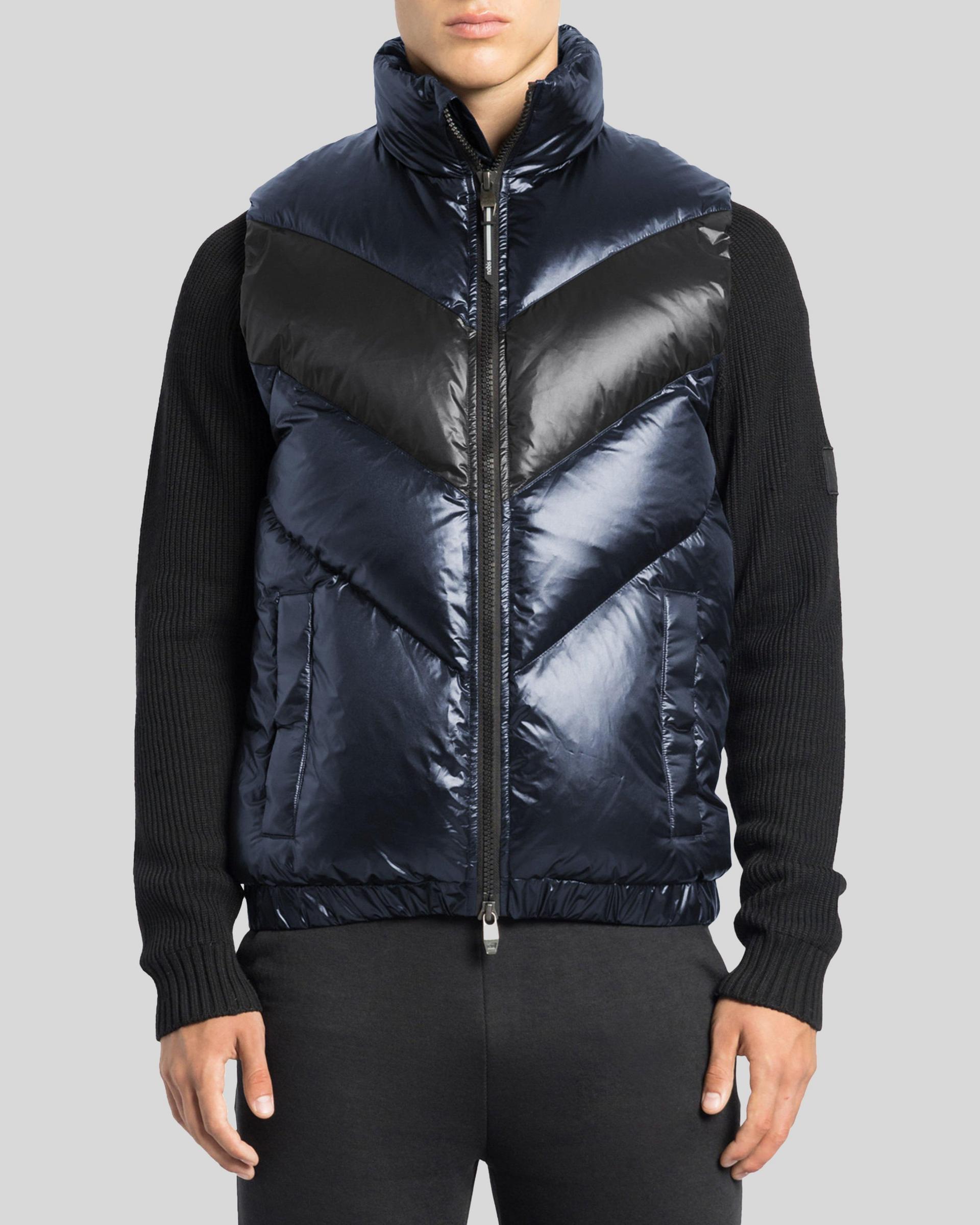 A male model wearing a metallic blue puffer vest styled with a black sweater