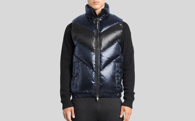 A male model wearing a metallic blue puffer vest styled with a black sweater