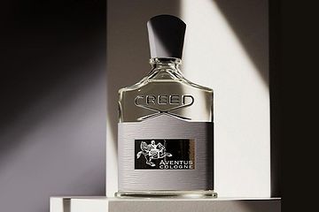 Image 27: A bottle of Creed Aventus cologne displayed on a white platform with dramatic lighting