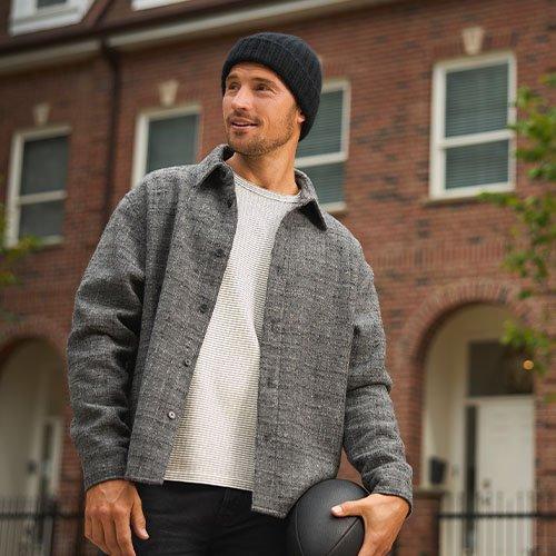 A man wearing a grey overshirt layered over a white t-shirt and black pants