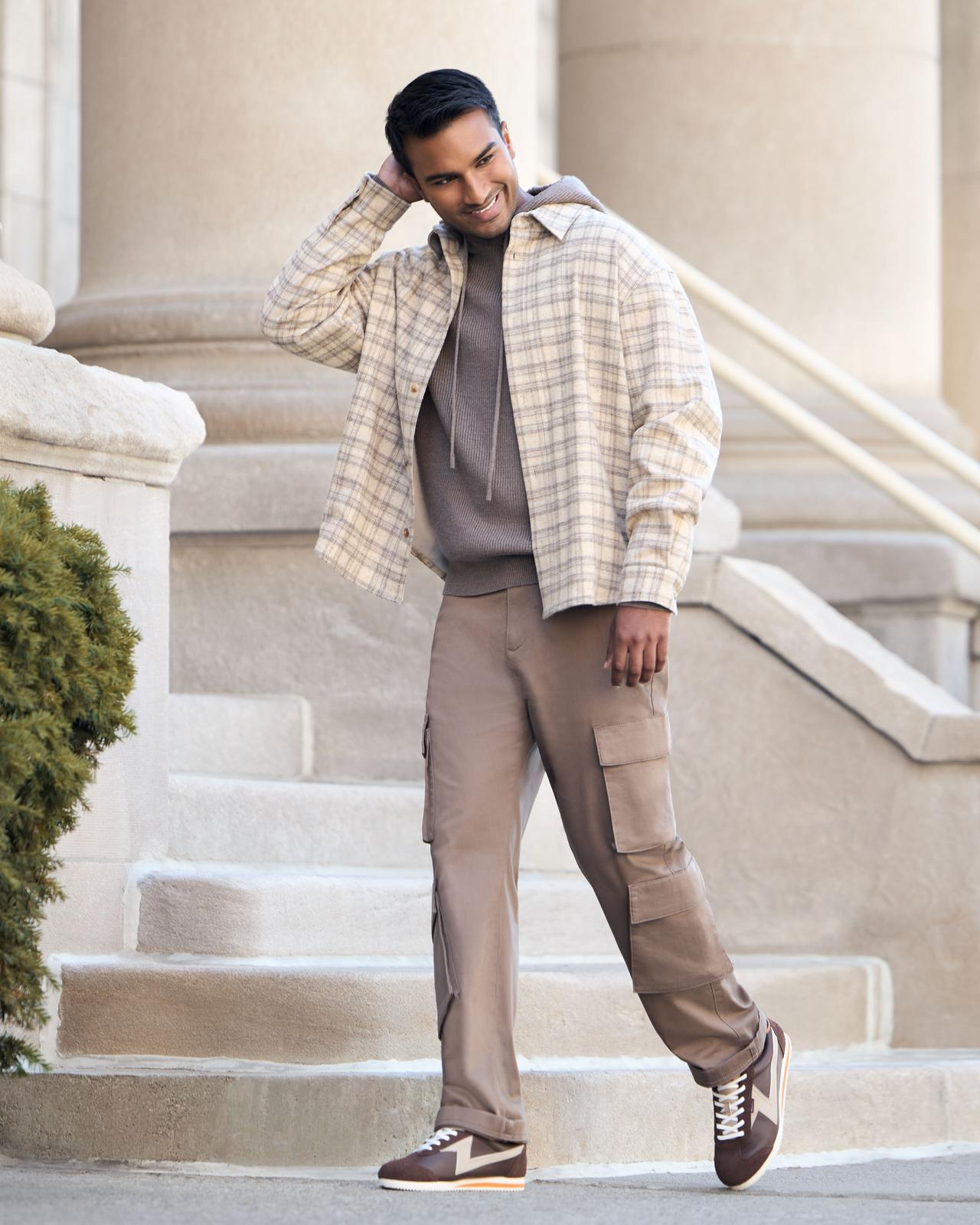 Homme portant une tenue décontractée avec une veste à carreaux, un pantalon cargo et des espadrilles, debout à l’extérieur