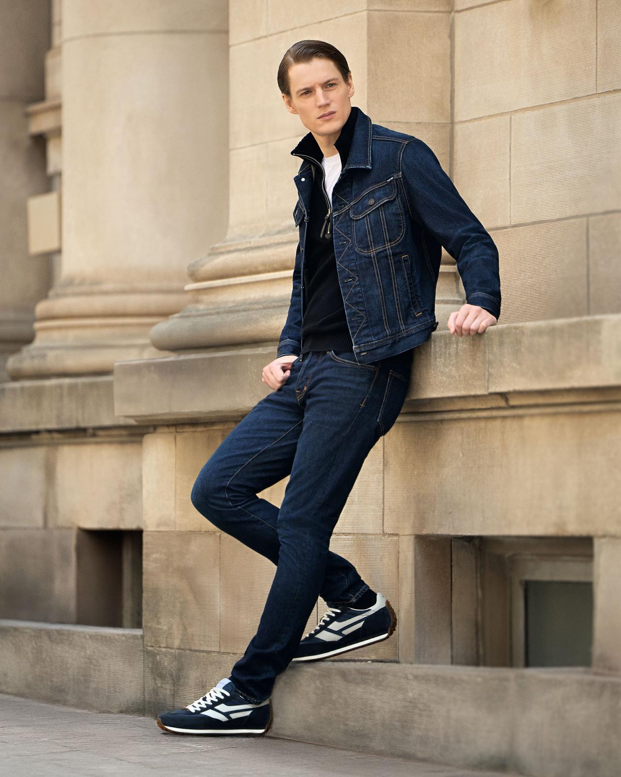 A man wearing a denim jacket layered over a white T-shirt with dark blue jeans