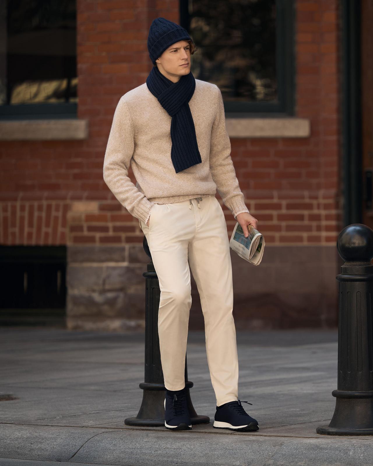 Un homme portant un chandail beige avec un pantalon crème, assorti d’une tuque, d’une écharpe et de chaussures de sport marine