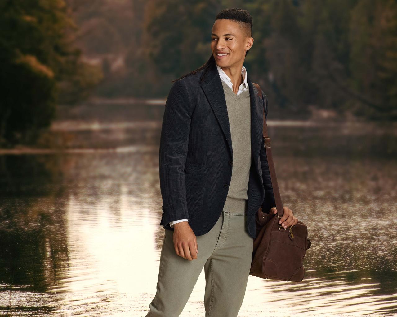 a man in a corduroy sport jacket standing on a dock near a lake