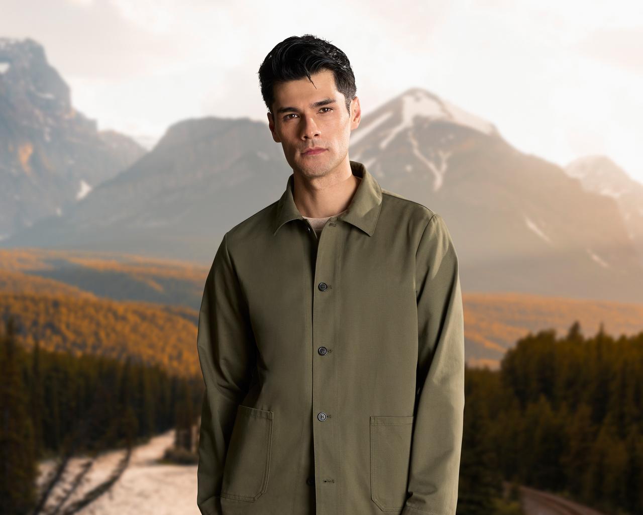 a man in a green jacket standing in front of a mountain range