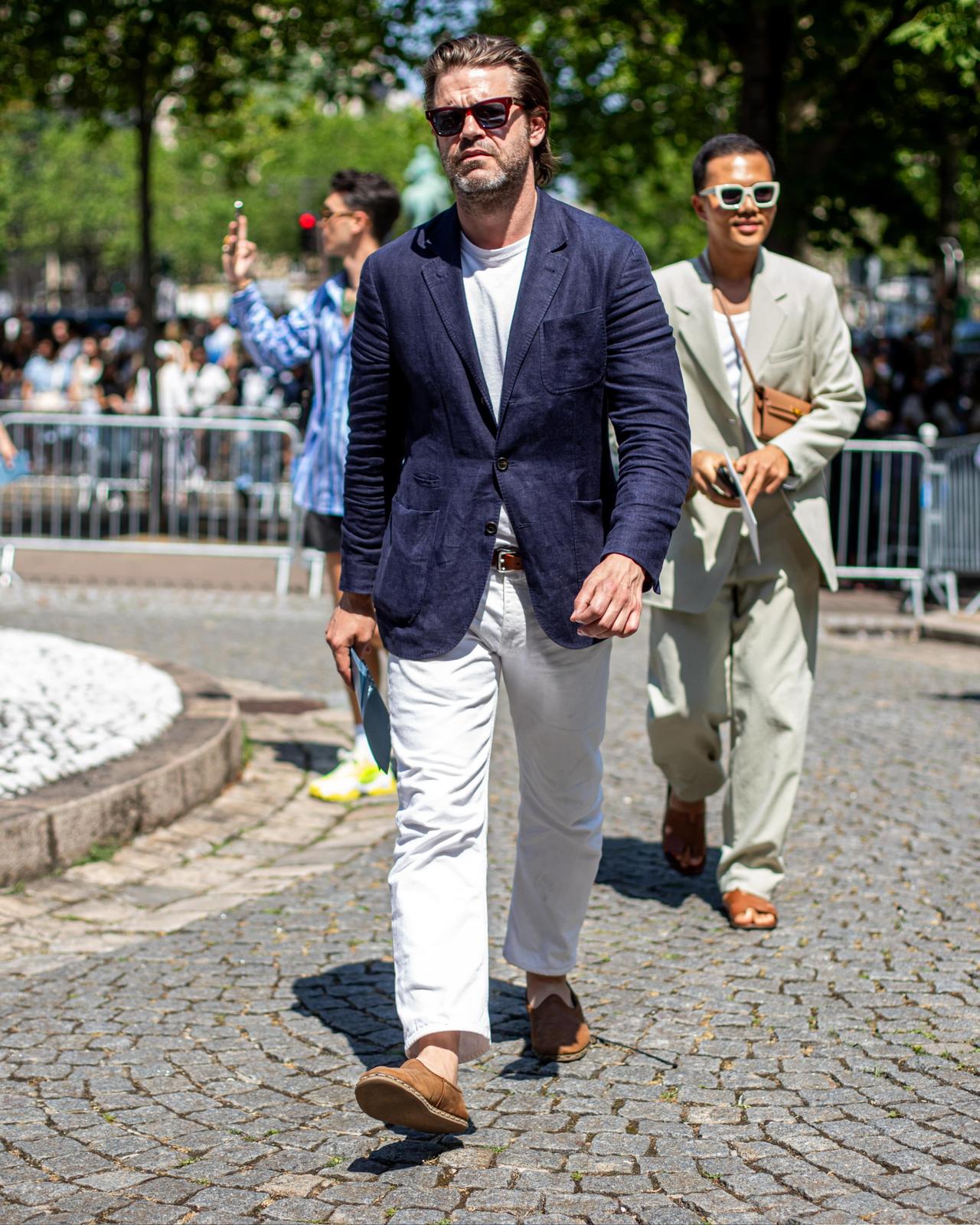 Homme en veston bleu marine, t-shirt blanc et pantalon blanc marchant à l’extérieur