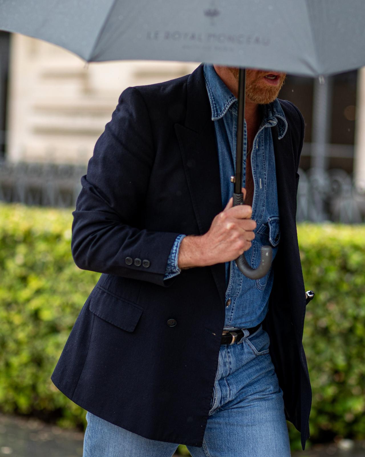Man in navy blazer, denim shirt and jeans walking outdoors