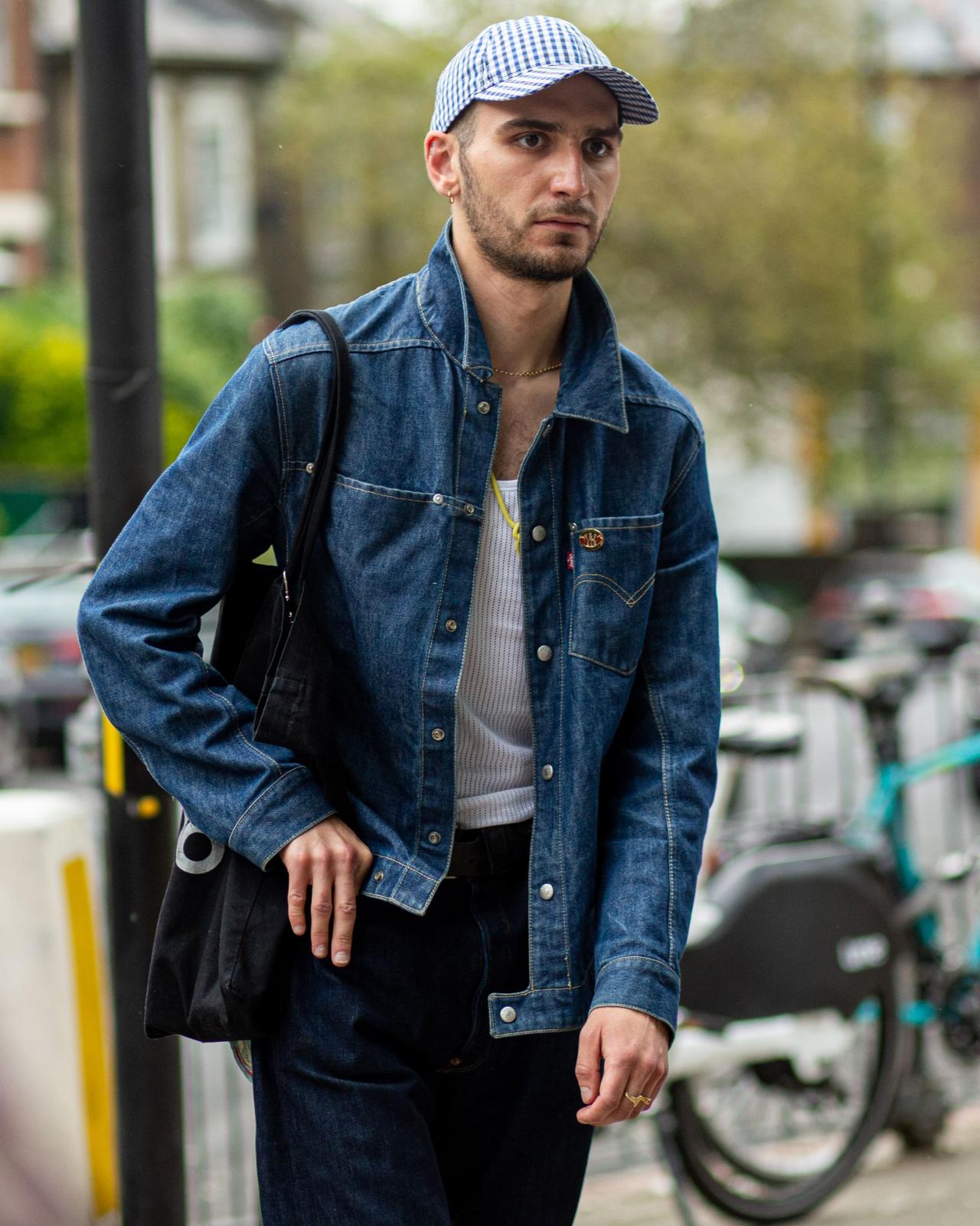 Man in blue denim oversized jacket layered over white tank top and black jeans