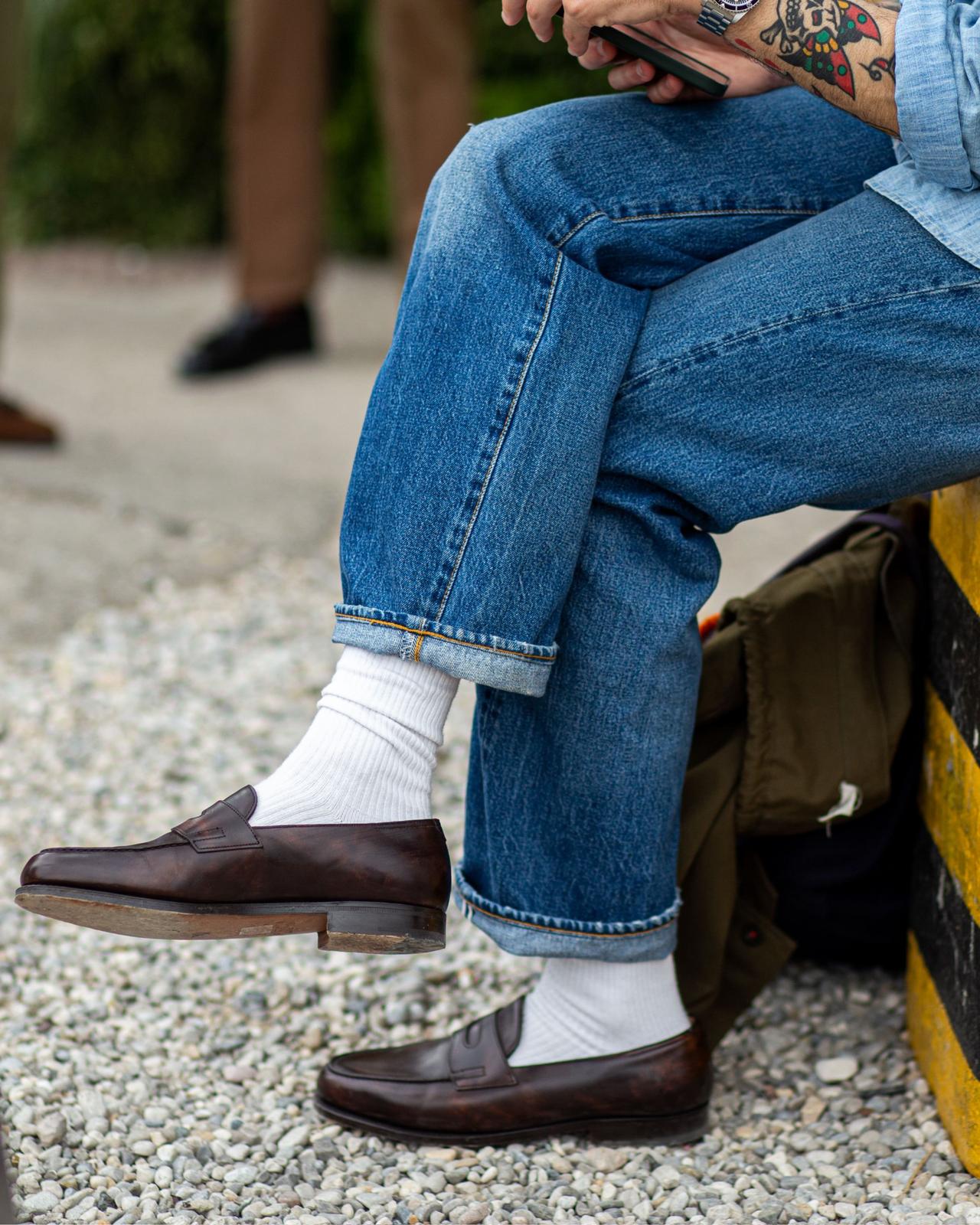 Man in dark denim jacket and jeans with white socks and brown leather loafers