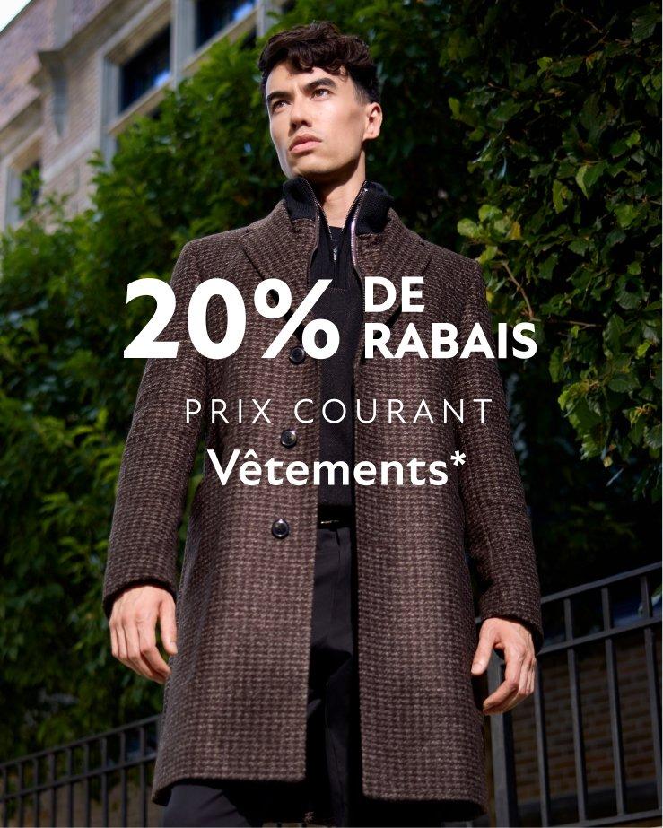 Un homme portant un manteau à carreaux bruns, avec un chandail noir et un pantalon noir