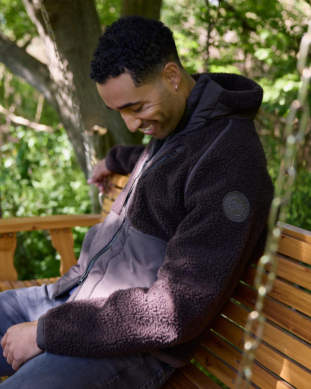 Man smiling while sitting outdoors in a dark brown sherpa fleece jacket, LW Outerwear microsite, FW26 collection