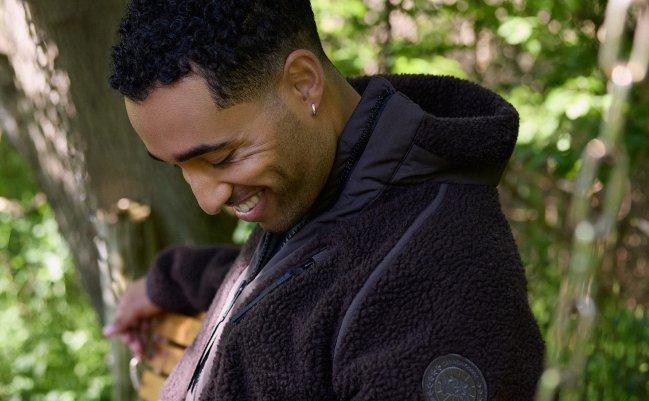 Homme souriant assis à l'extérieur, portant une veste en molleton sherpa brun foncé, microsite LW Outerwear, collection A/H26