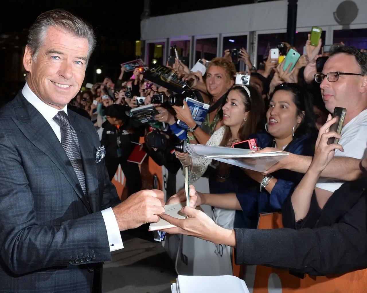 The actor is dressed in a dark checkered suit and tie, engaging warmly with supporters as they take photos and autographs