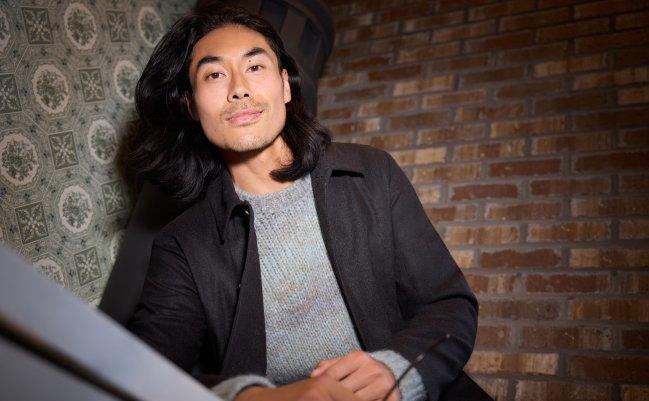 Model wearing a light grey knit sweater layered under a dark blazer