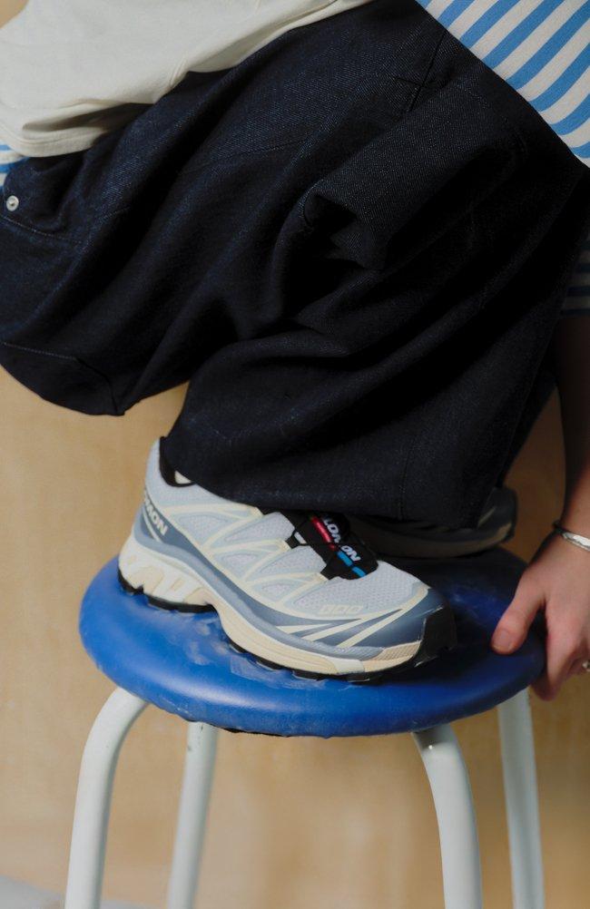 Man wearing white and blue Salomon sneakers, resting his foot on a blue stool