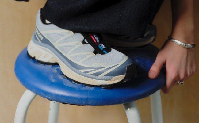 Man wearing white and blue Salomon sneakers, resting his foot on a blue stool