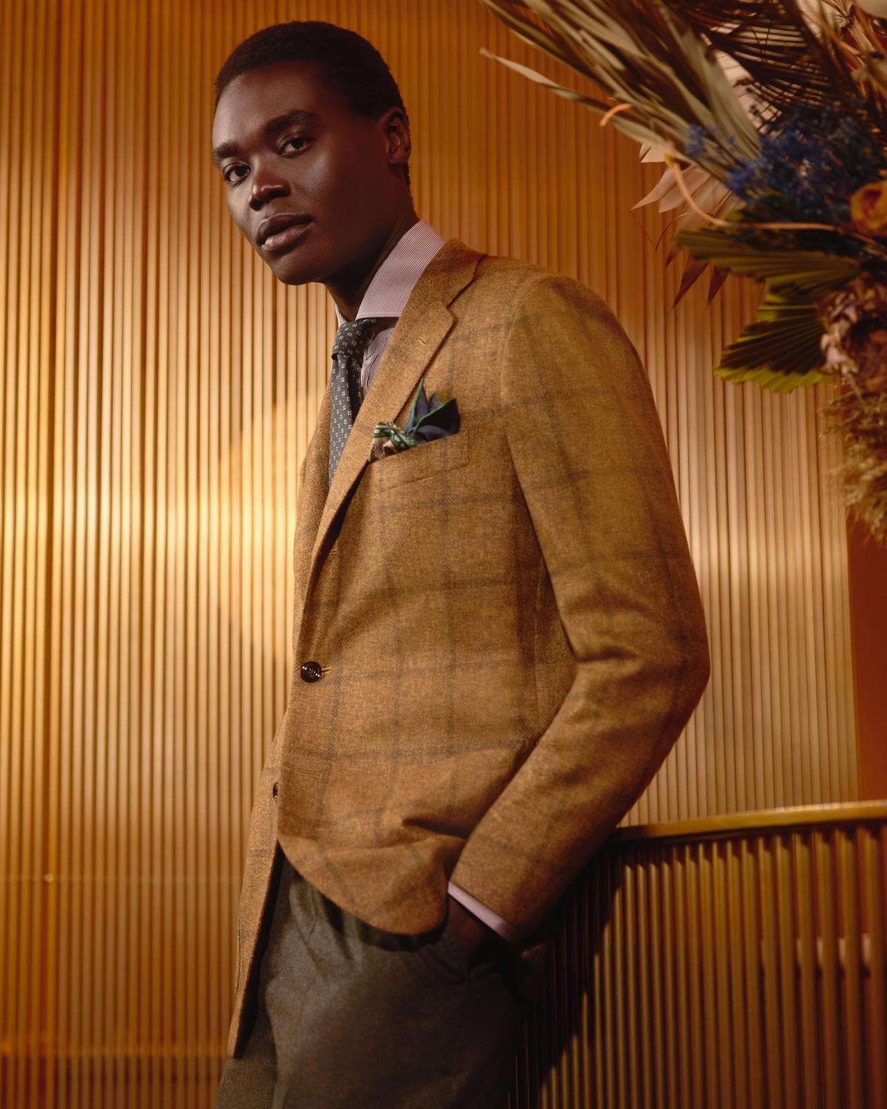 Un homme portant une veste brun fauve, agencée à une chemise rose pâle, une cravate à motifs et une boutonnière verte