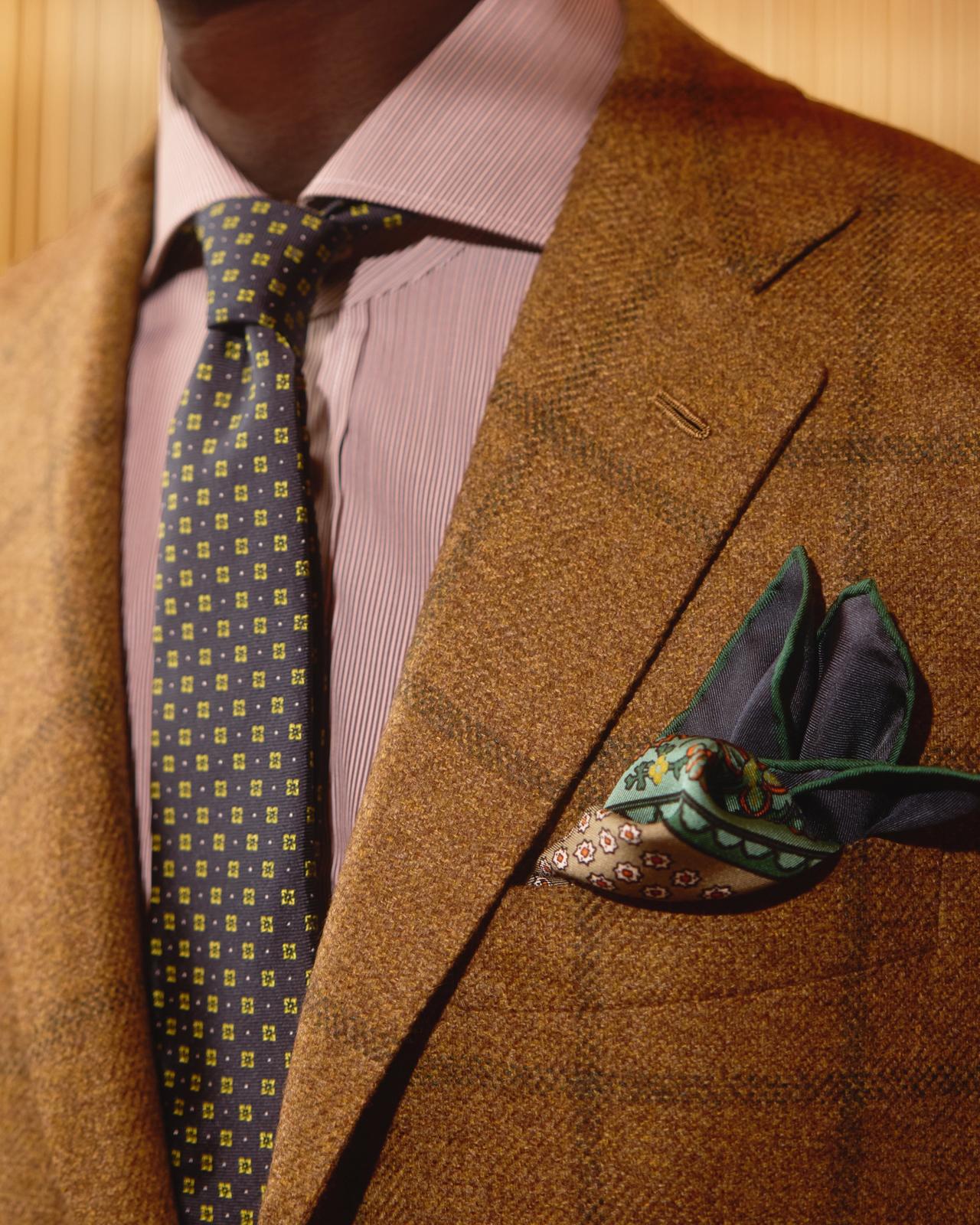Un complet ajusté en tweed brun, agencé à une cravate à motifs et à une pochette de costume décorative
