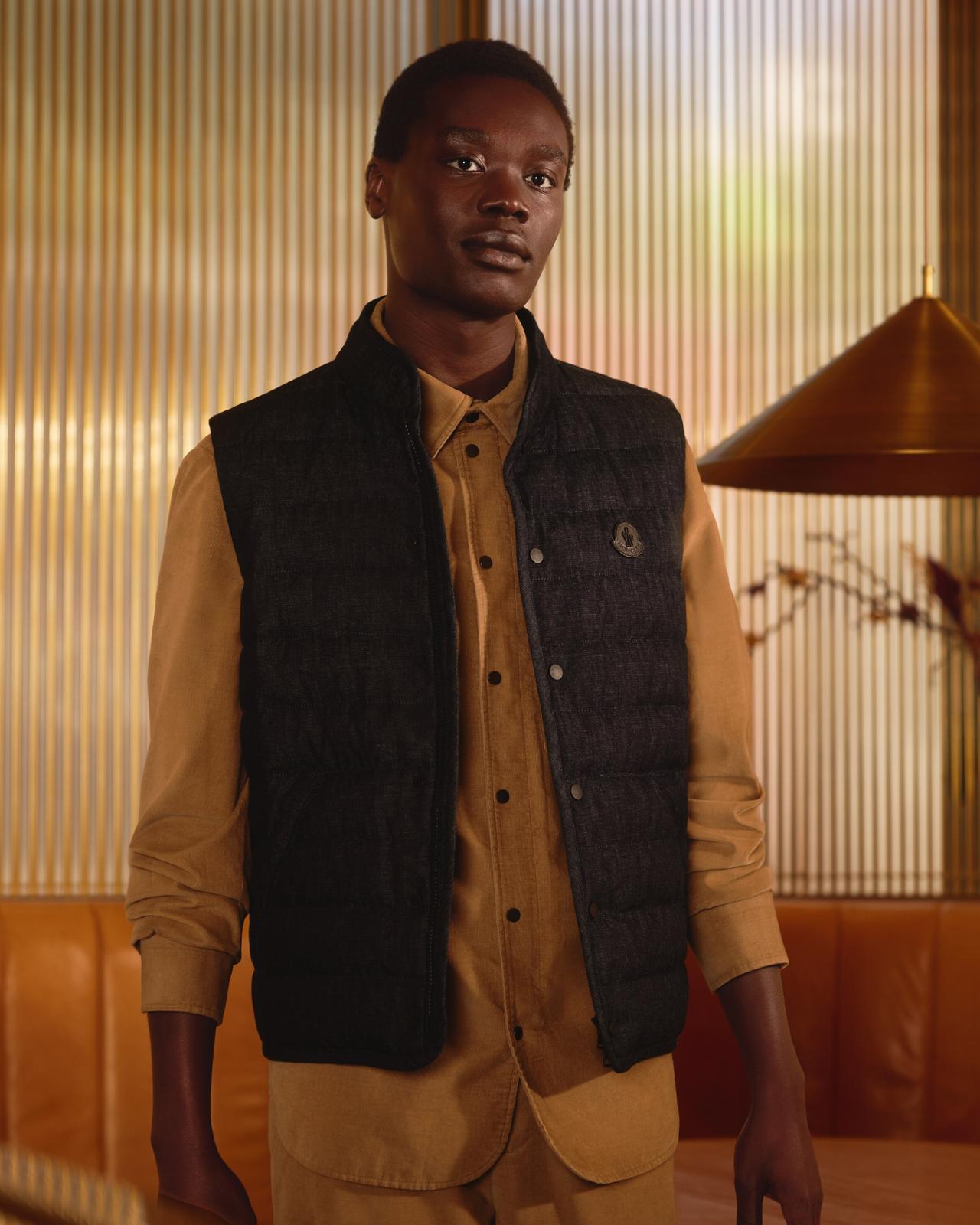 A model wearing a padded gilet in black, paired with a mustard-colored button-up shirt