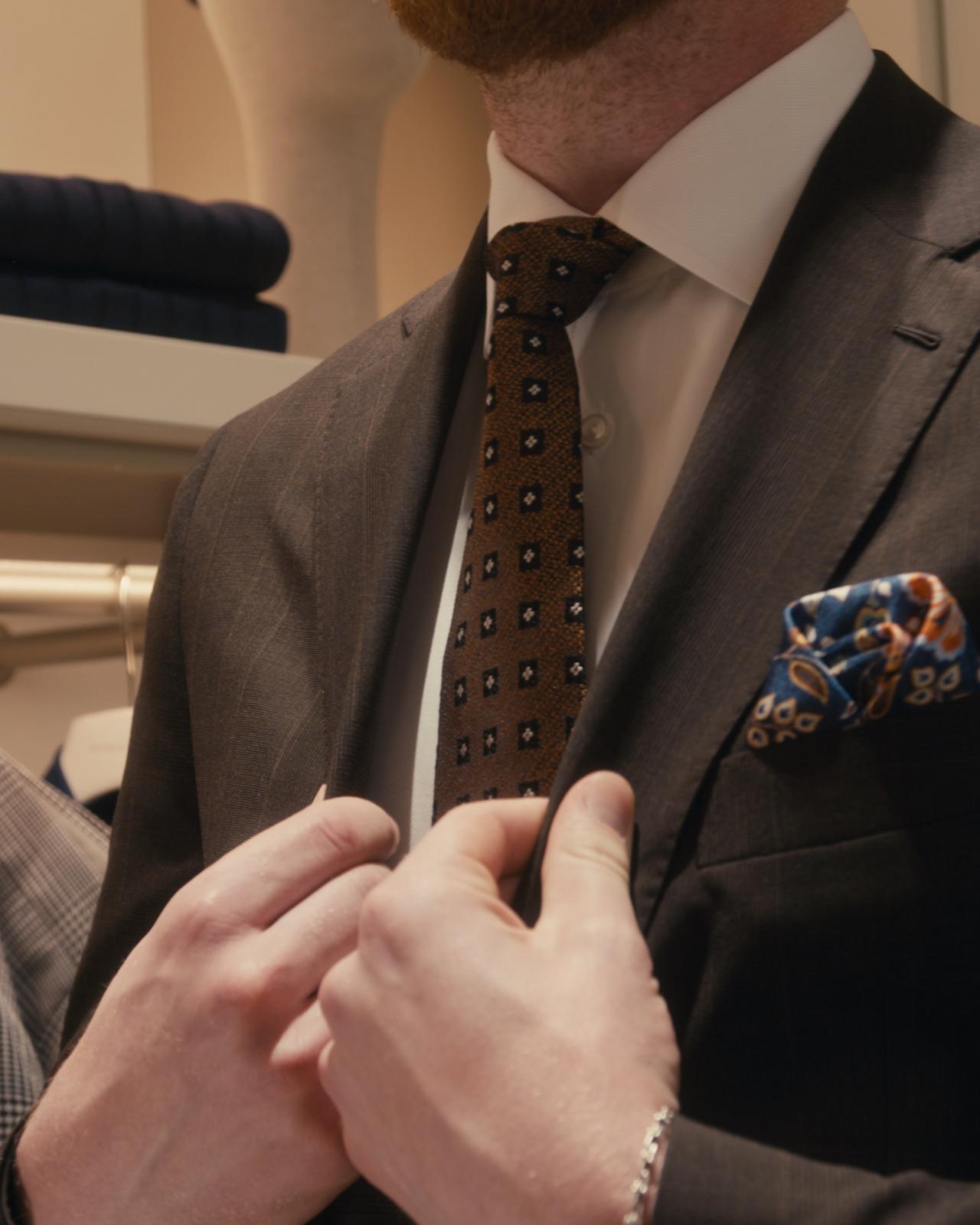 Luke Prokop wearing a alight grey suit with white shirt, dark brown tie and printed pocket square