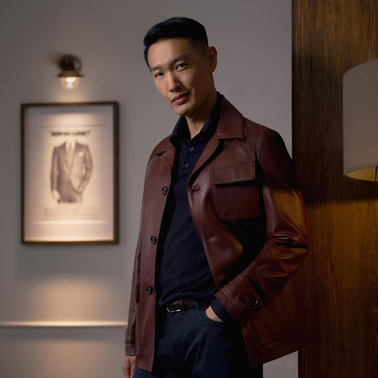 Un homme portant une veste en cuir brune avec un polo bleu foncé et un pantalon bleu foncé