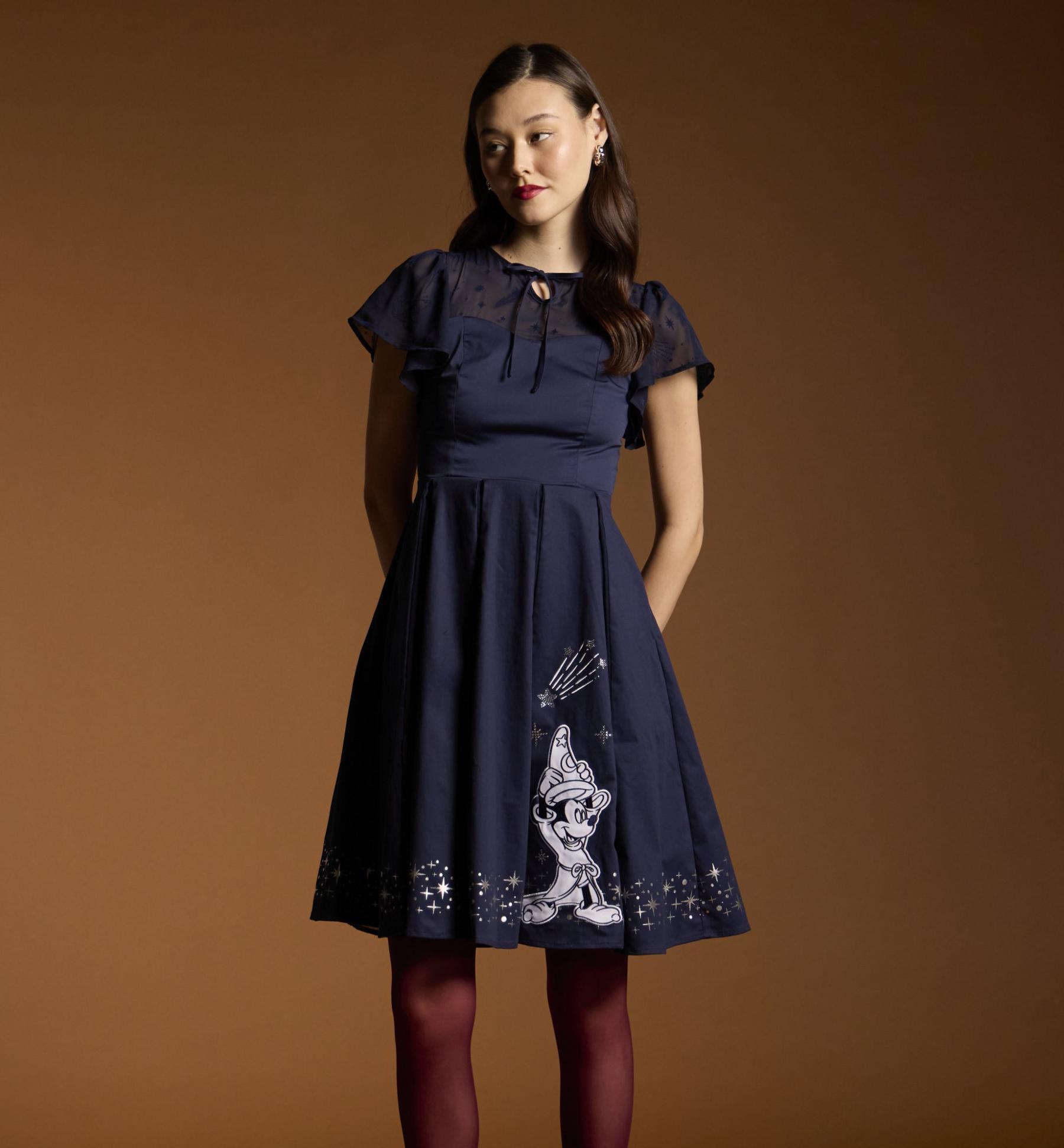 Model wearing a navy dress with sheer flutter sleeves and Mickey Mouse print skirt. Shop now.