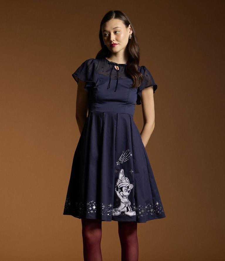 Model wearing a navy dress with sheer flutter sleeves and Sorcerer Mickey print skirt. Shop now.