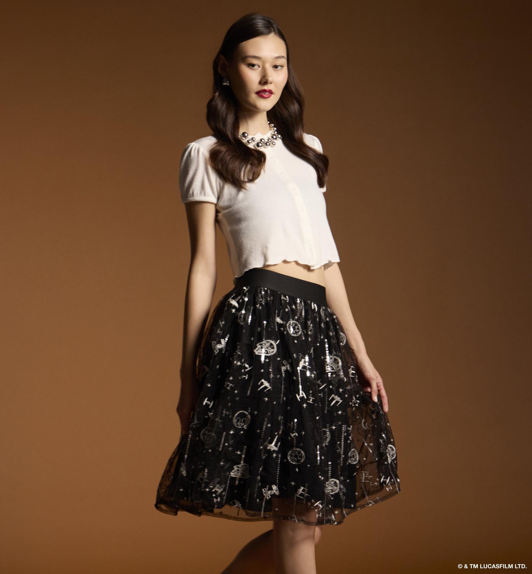 Model wearing a white short-sleeve cropped cardigan and black patterned tulle skirt. Shop retro fashion.