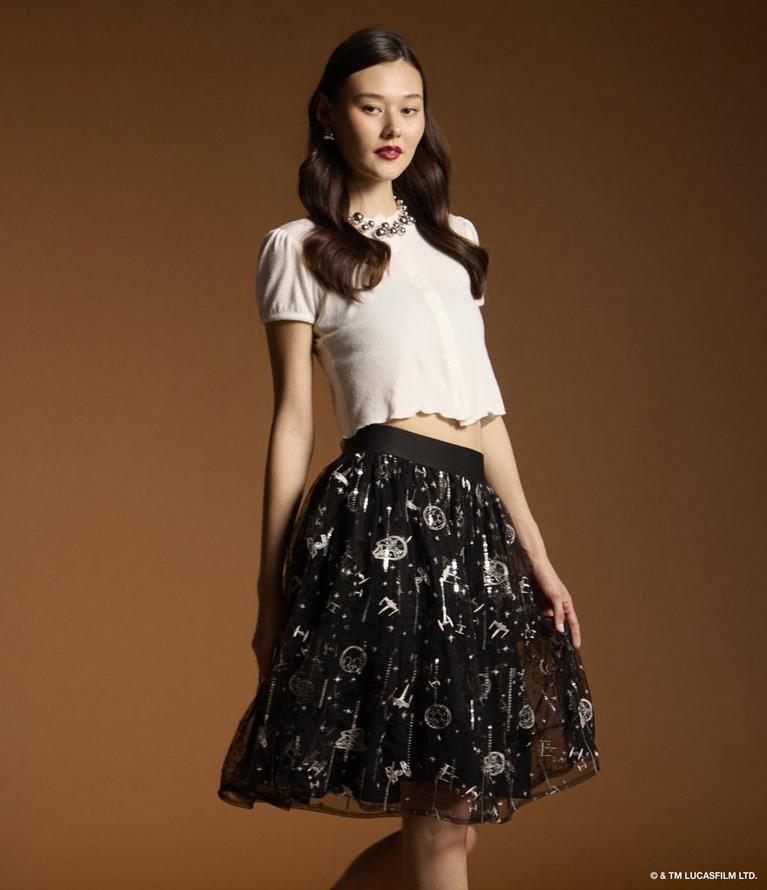 Model wearing a white short-sleeve top with a black embellished skirt and statement necklace. Shop retro fashion.