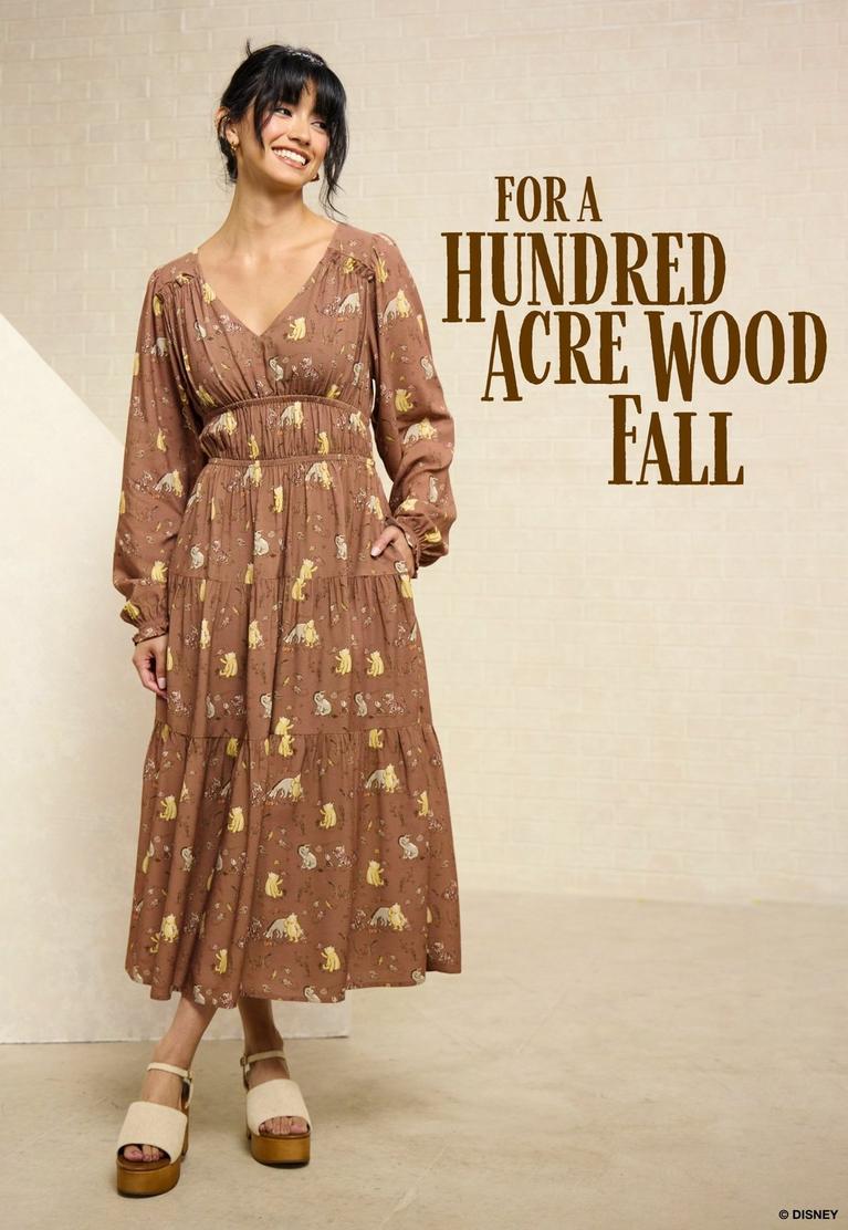 Model wearing a brown long-sleeve printed midi dress, with text “FOR A HUNDRED ACRE WOOD FALL”. Shop Winnie the Pooh.