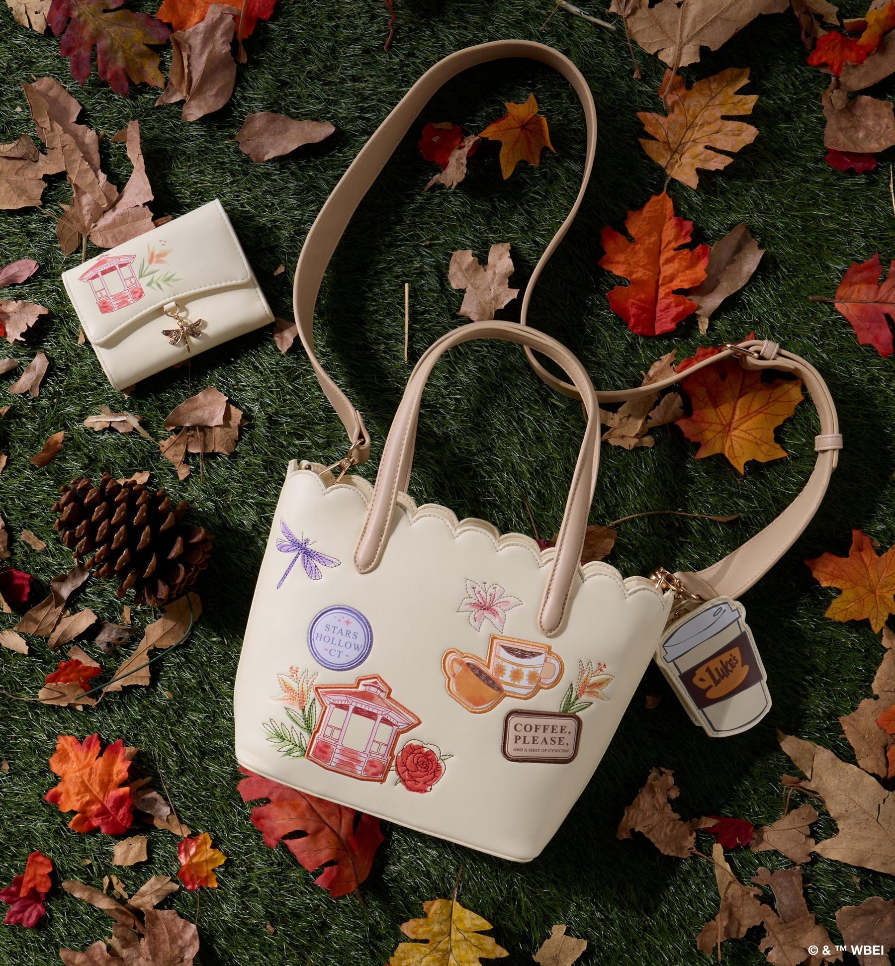 Cream tote bag with themed patches and matching wallet, shown on grass with fall leaves. Shop bags.