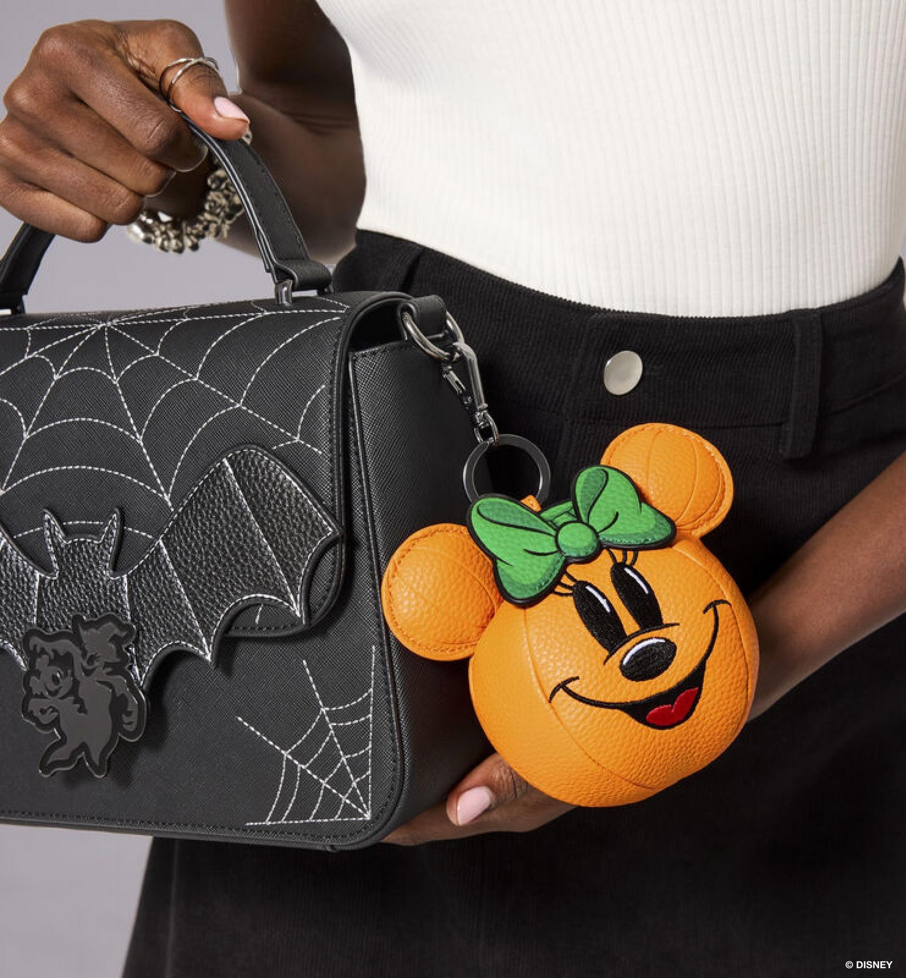 Person holding a black spiderweb handbag with Minnie Mouse pumpkin coin purse charm. Shop bags.