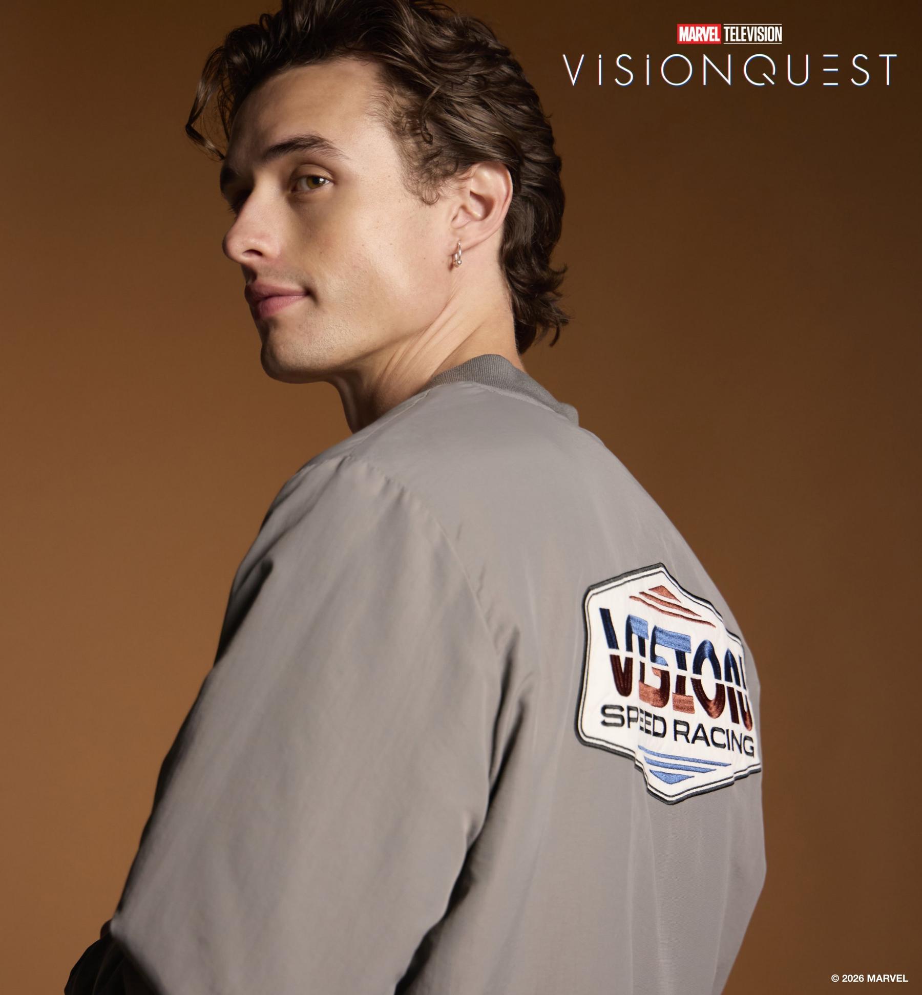 Man in gray jacket with “VISION SPEED RACING” patch and “MARVEL TELEVISION VISIONQUEST” text. Shop VisionQuest collection.