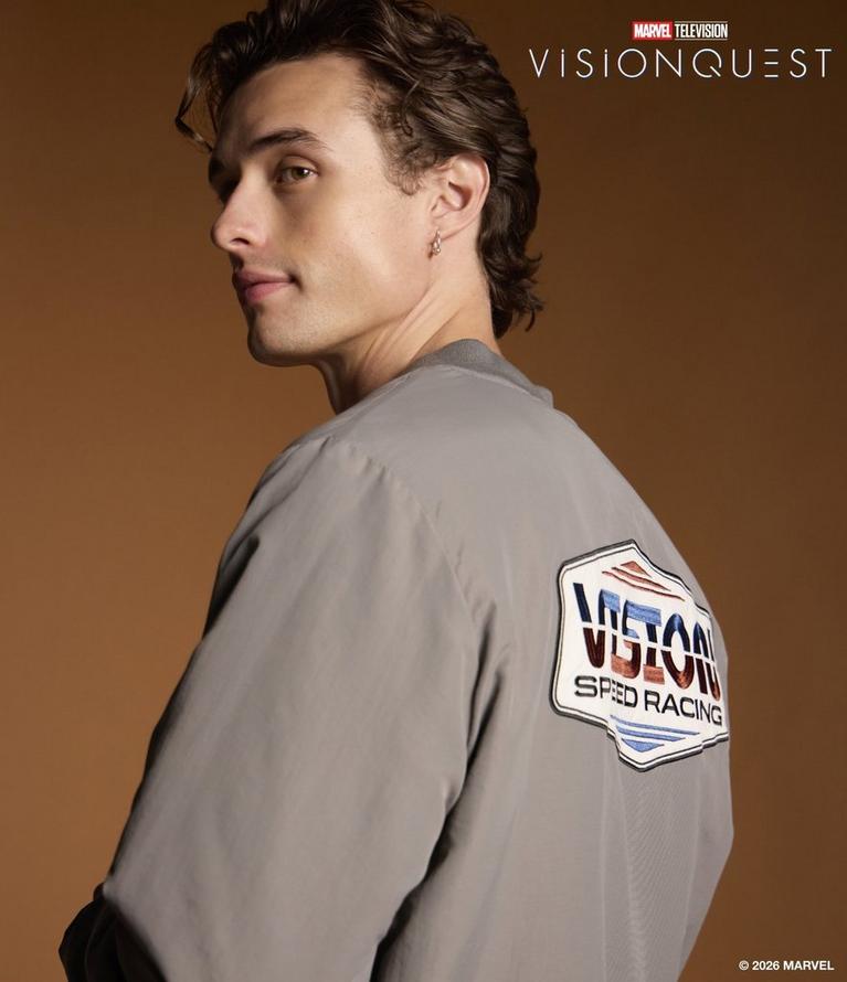 Man in gray jacket with “Vision Speed Racing” patch; Marvel Television Vision Quest text. Shop VisionQuest collection.