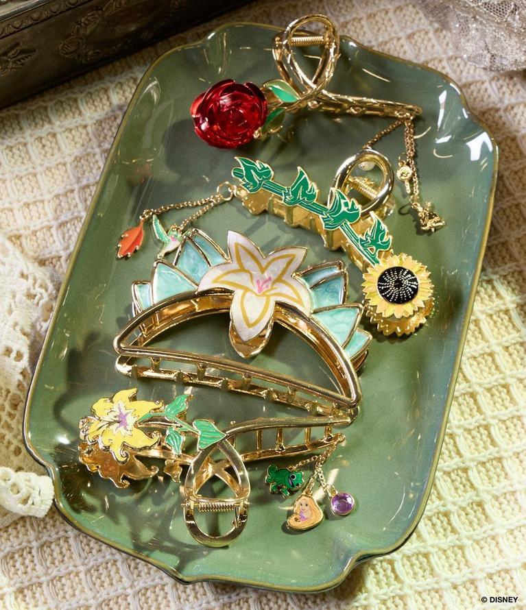 Gold-tone floral hair claw clips and charms arranged on a green dish. Shop hair accessories.