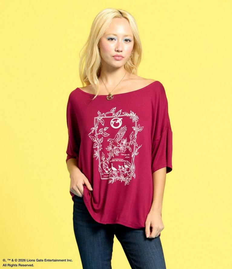 Model wearing burgundy off-shoulder top with white bird and floral graphic print. Shop The Hunger Games.