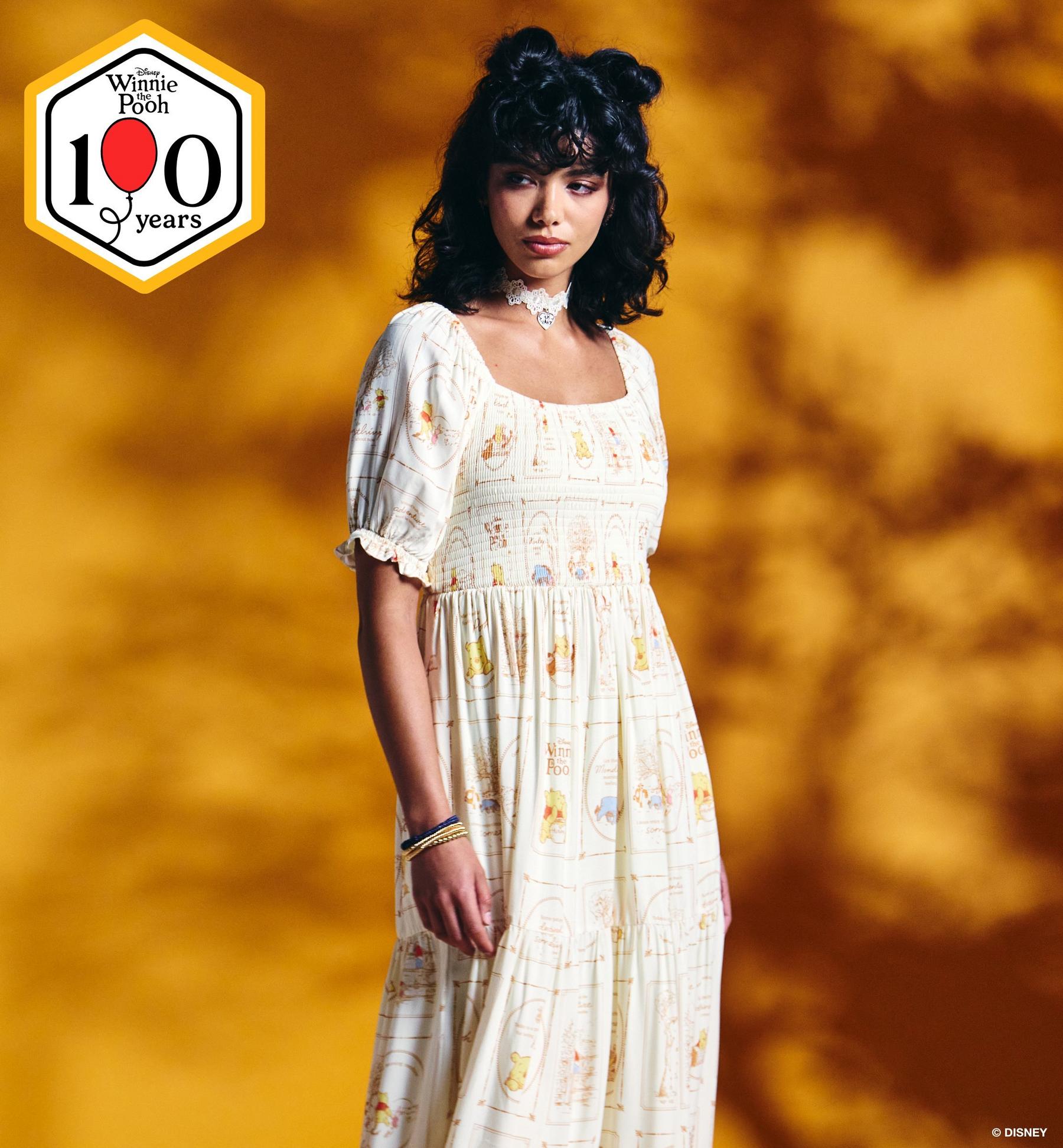 Model wearing a Disney Winnie the Pooh print dress with “Winnie the Pooh 100 years” badge. Shop Winnie the Pooh collection.