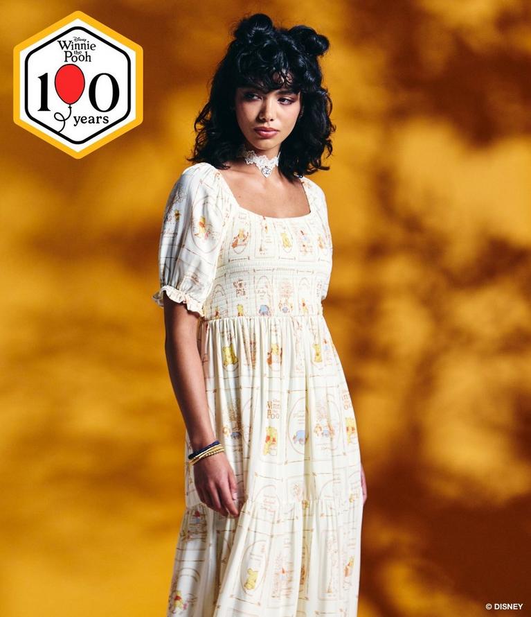Model wearing a Winnie the Pooh print dress and lace choker, with Disney 100 years badge. Shop Winnie The Pooh collection.