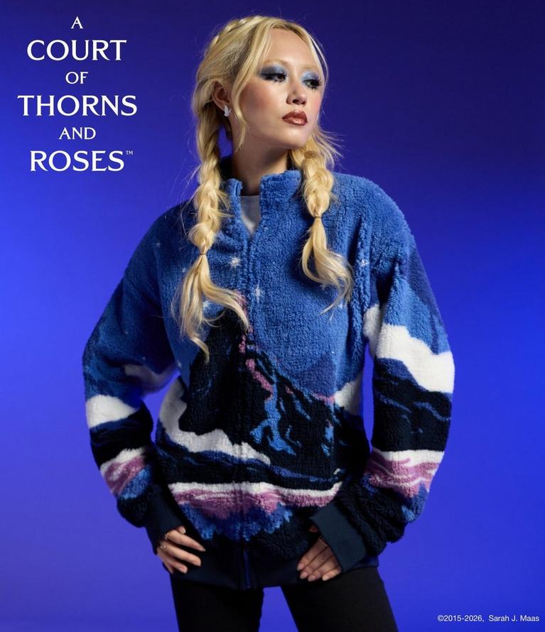 Model wearing a blue fleece zip-up jacket with graphic print and “A Court of Thorns and Roses” text. Shop A Court of Thorns and Roses collection.
