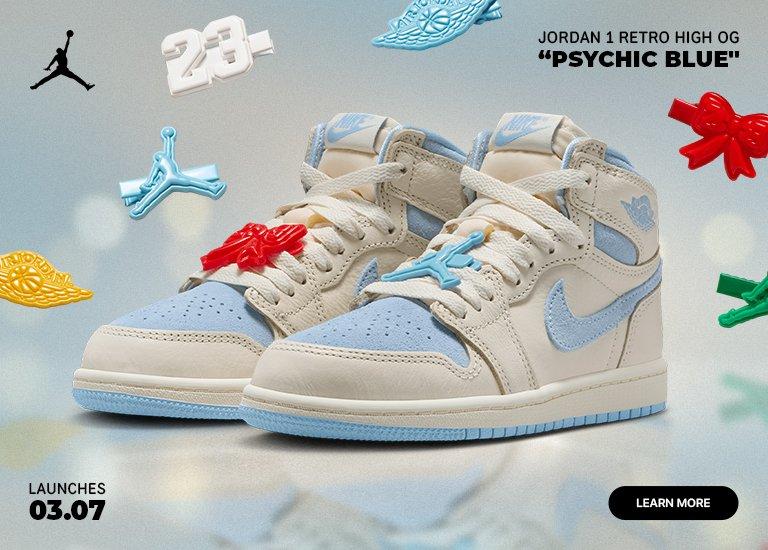 A promotional image for the Jordan 1 Retro High OG Psychic Blue showcasing a pair of cream-colored high-top sneakers with light blue suede accents on the toe, swoosh, and collar. The shoes are accessorized with colorful hair clips on the laces, surrounded by floating versions of those clips including the Jumpman logo, a red bow, and the number 23. The text states a launch date of 03.07.