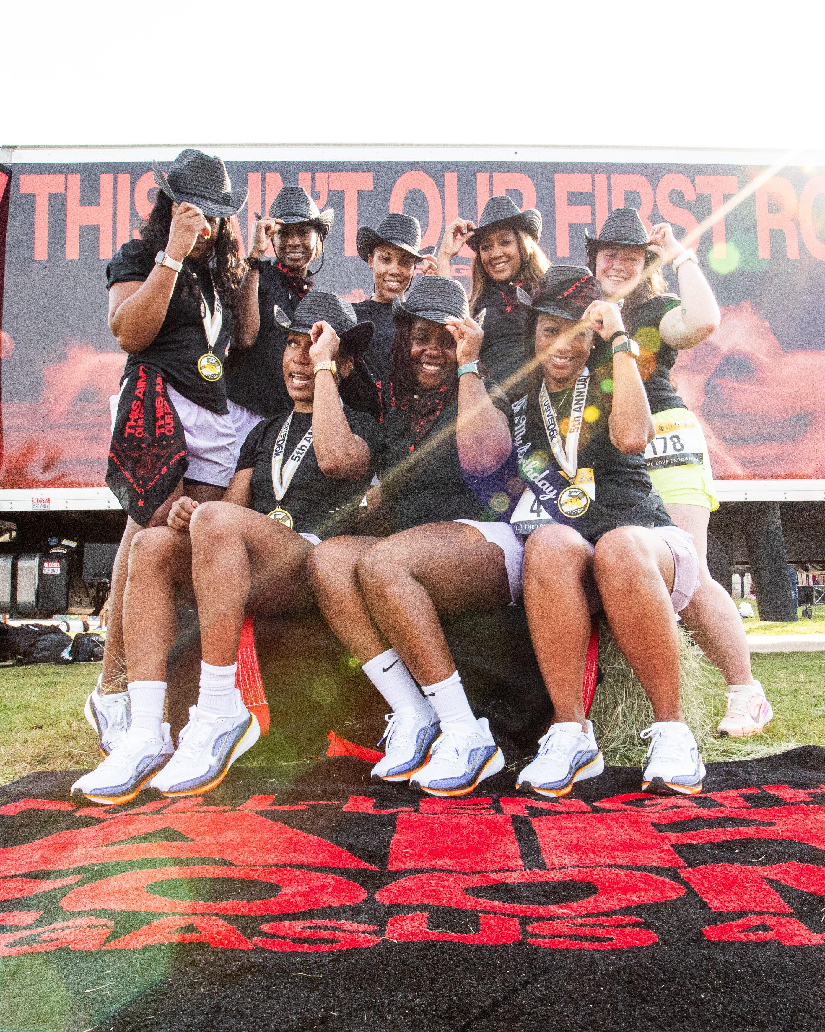 A group of women runners wearing medals and matching hats pose together after a race, showcasing community and team spirit at the event.